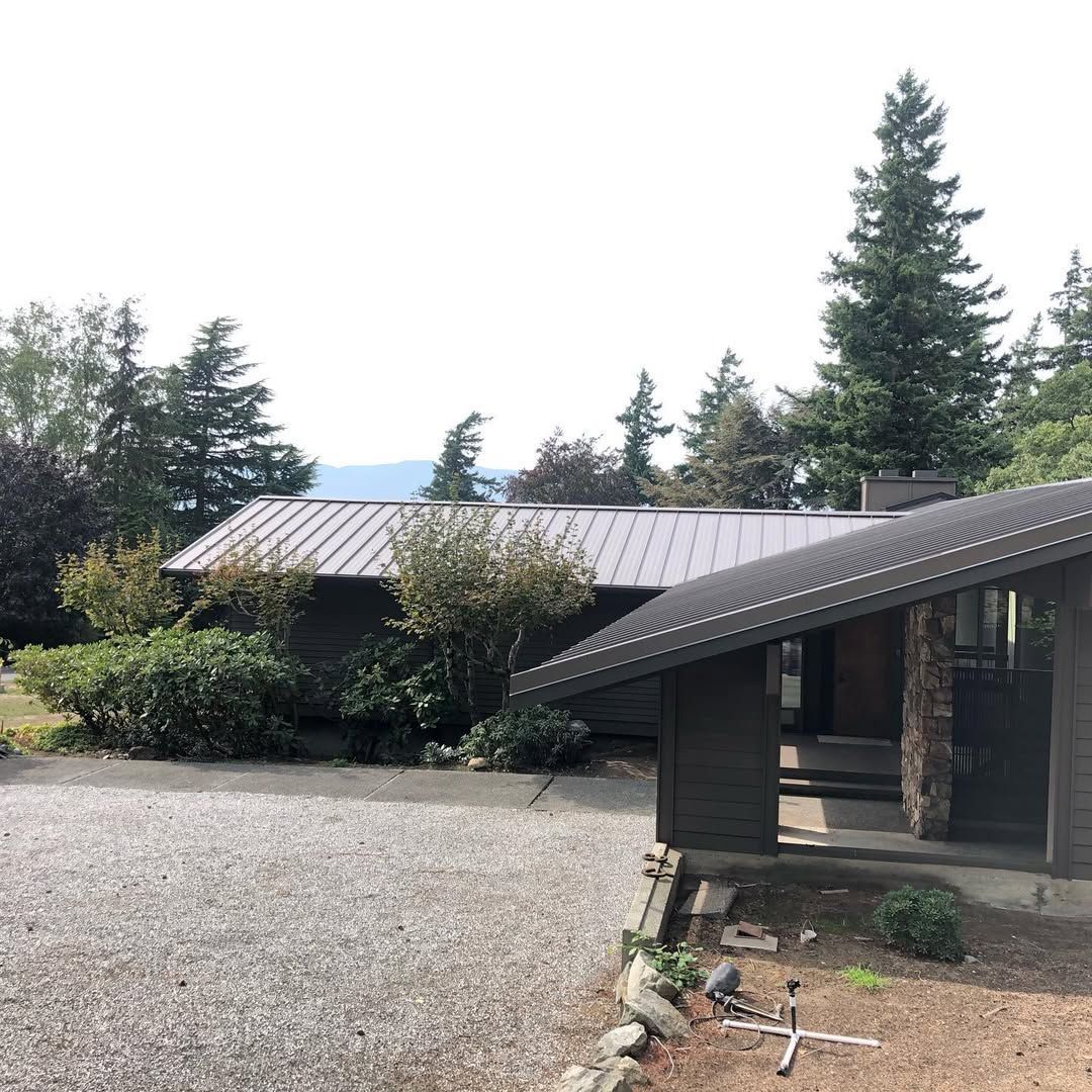 A house with a metal roof is surrounded by trees and gravel.